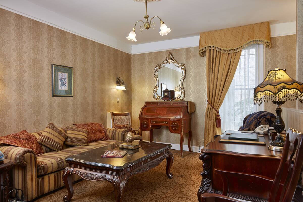 A traditional room with a sofa, a desk, a lamp, and a mirror.