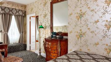 A room with floral wallpaper, a wooden dresser, a bench, and a bed with patterned bedding.