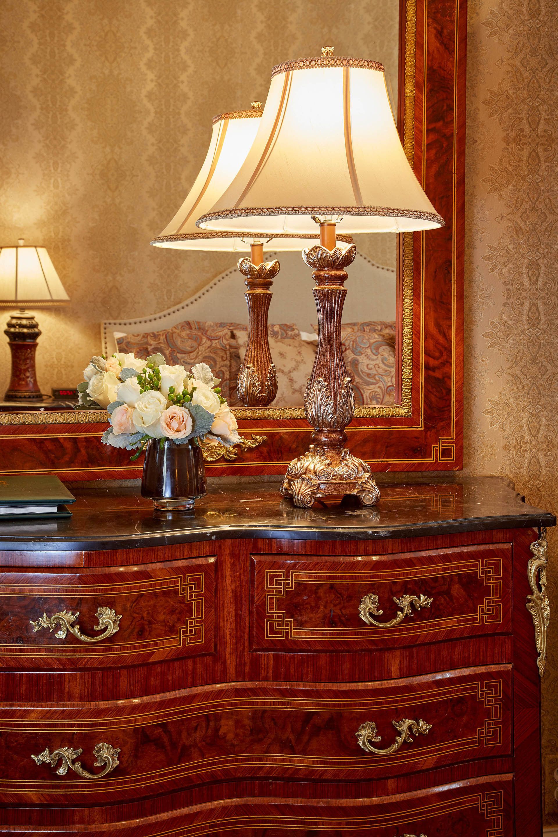 A wooden dresser with ornate handles and a vase of flowers.