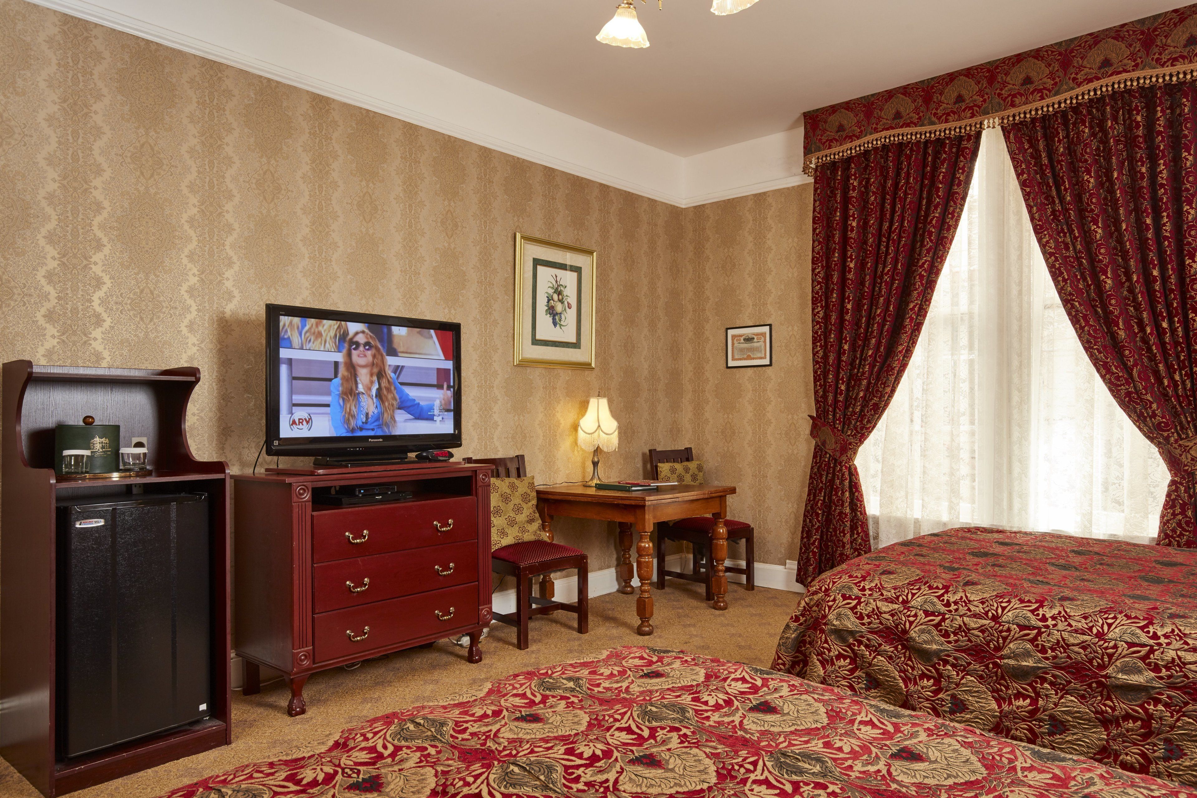 Ein Hotelzimmer mit Fernseher, Schreibtisch, Stuhl, Bett und Teppichboden.