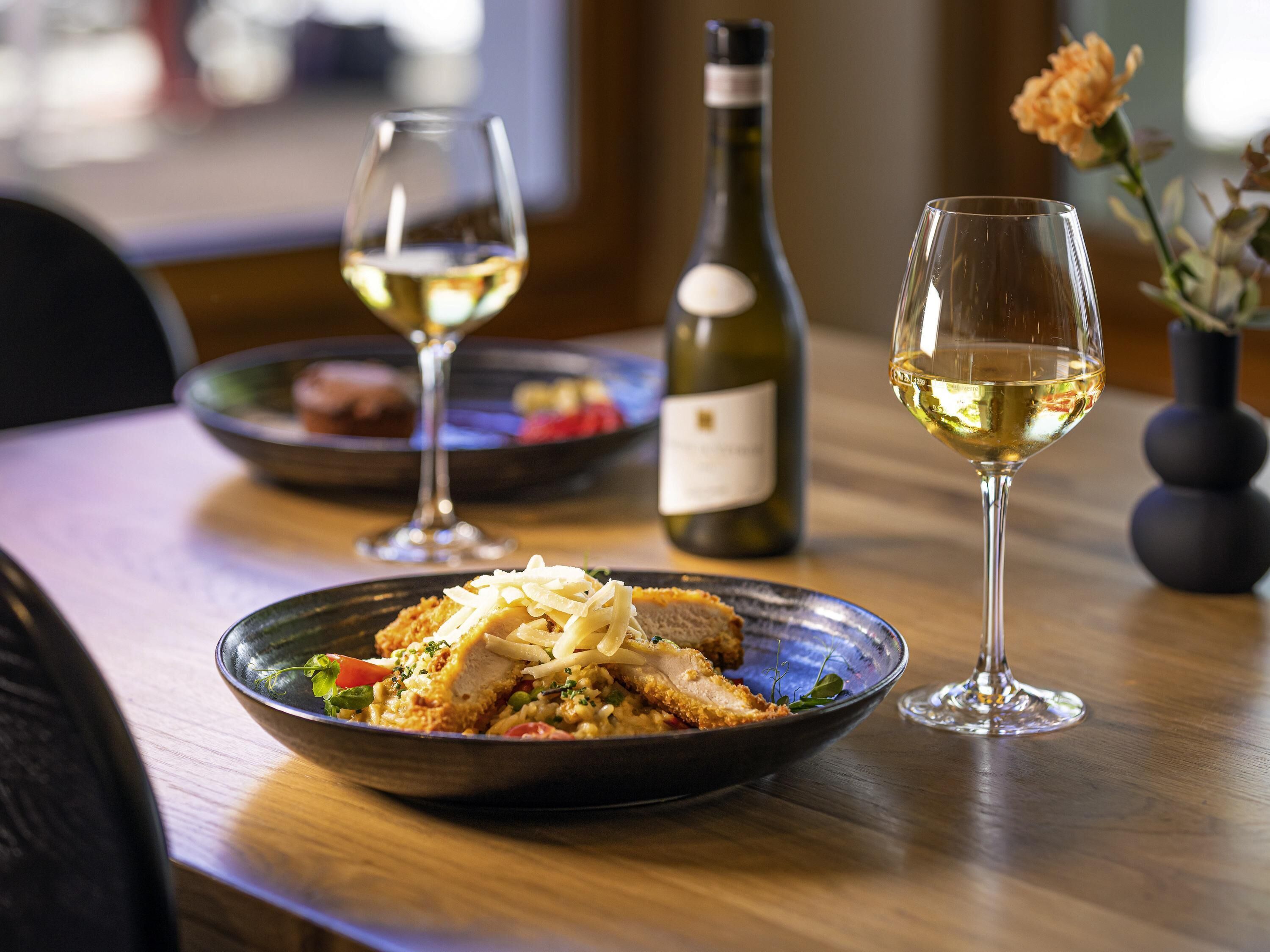 A dining table with a plate of food, two wine glasses, and a bottle of wine.