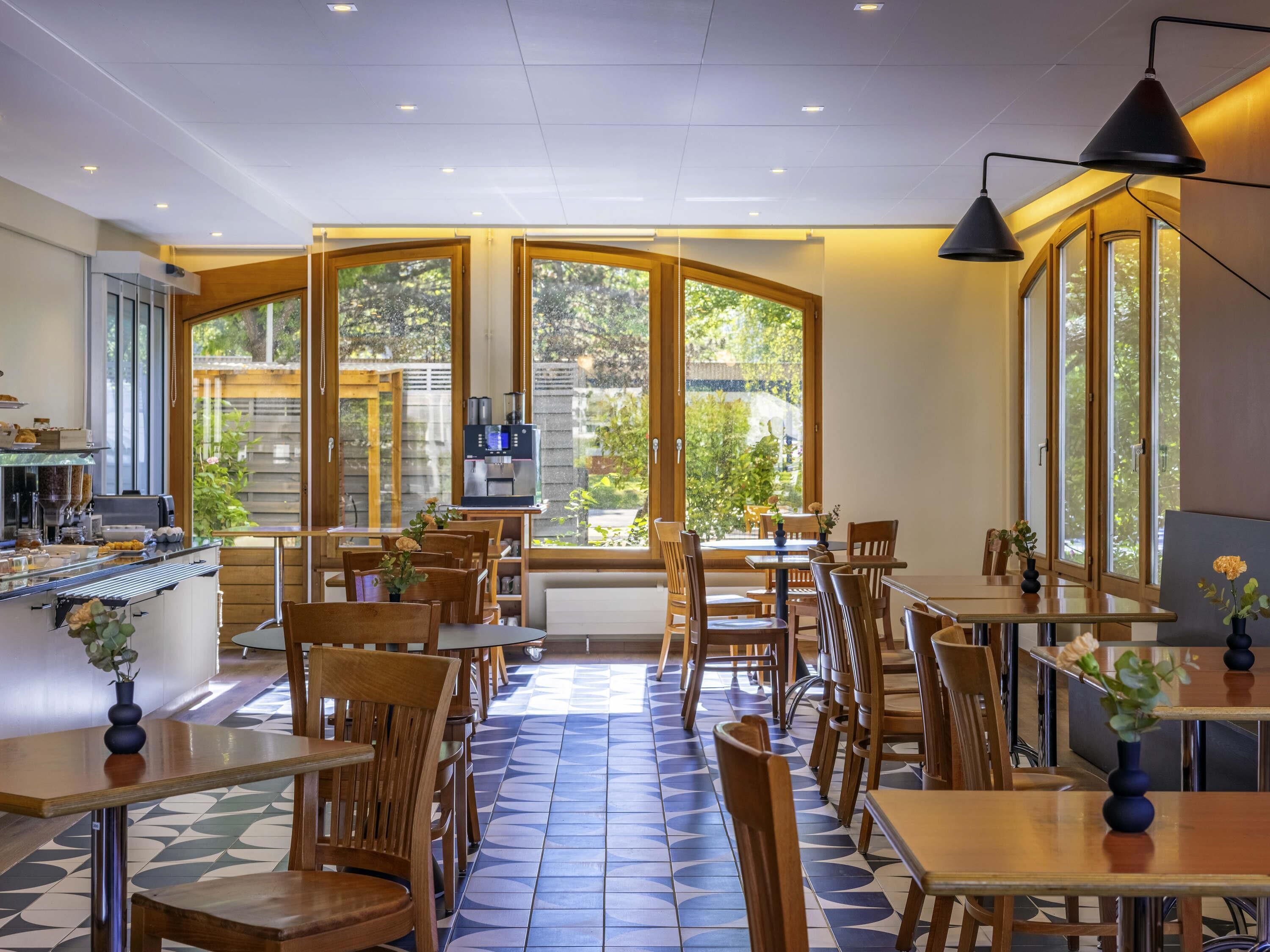 A cafe with wooden furniture, large windows, and a coffee machine.