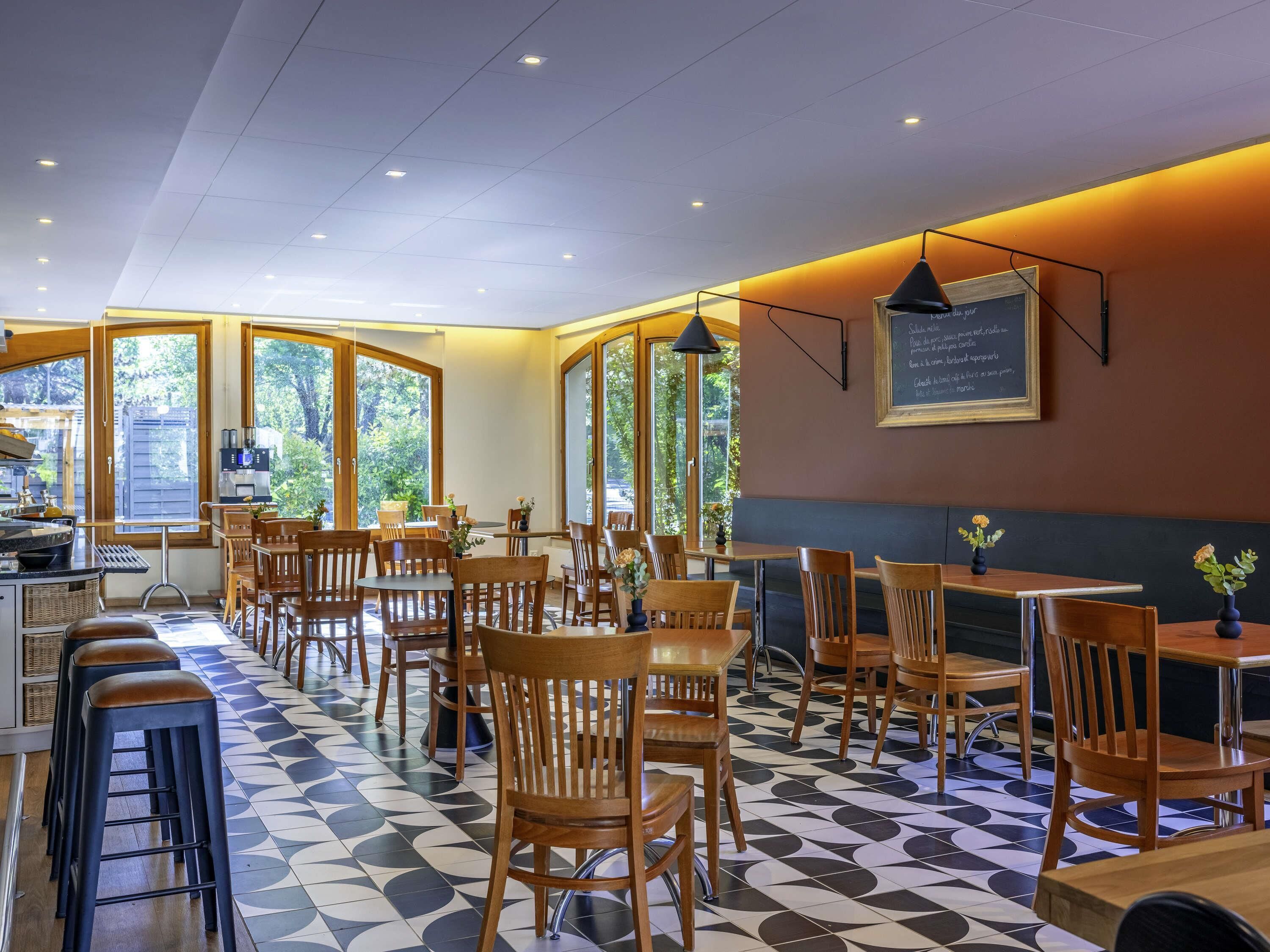 Ein Restaurant mit Schachbrettboden, Holztischen und -stühlen und großen Fenstern.