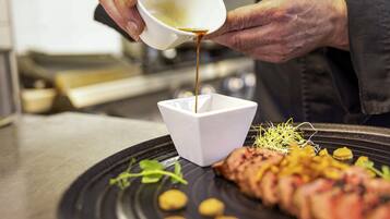 Une personne verse de la sauce dans un bol blanc posé sur une assiette contenant de la nourriture.