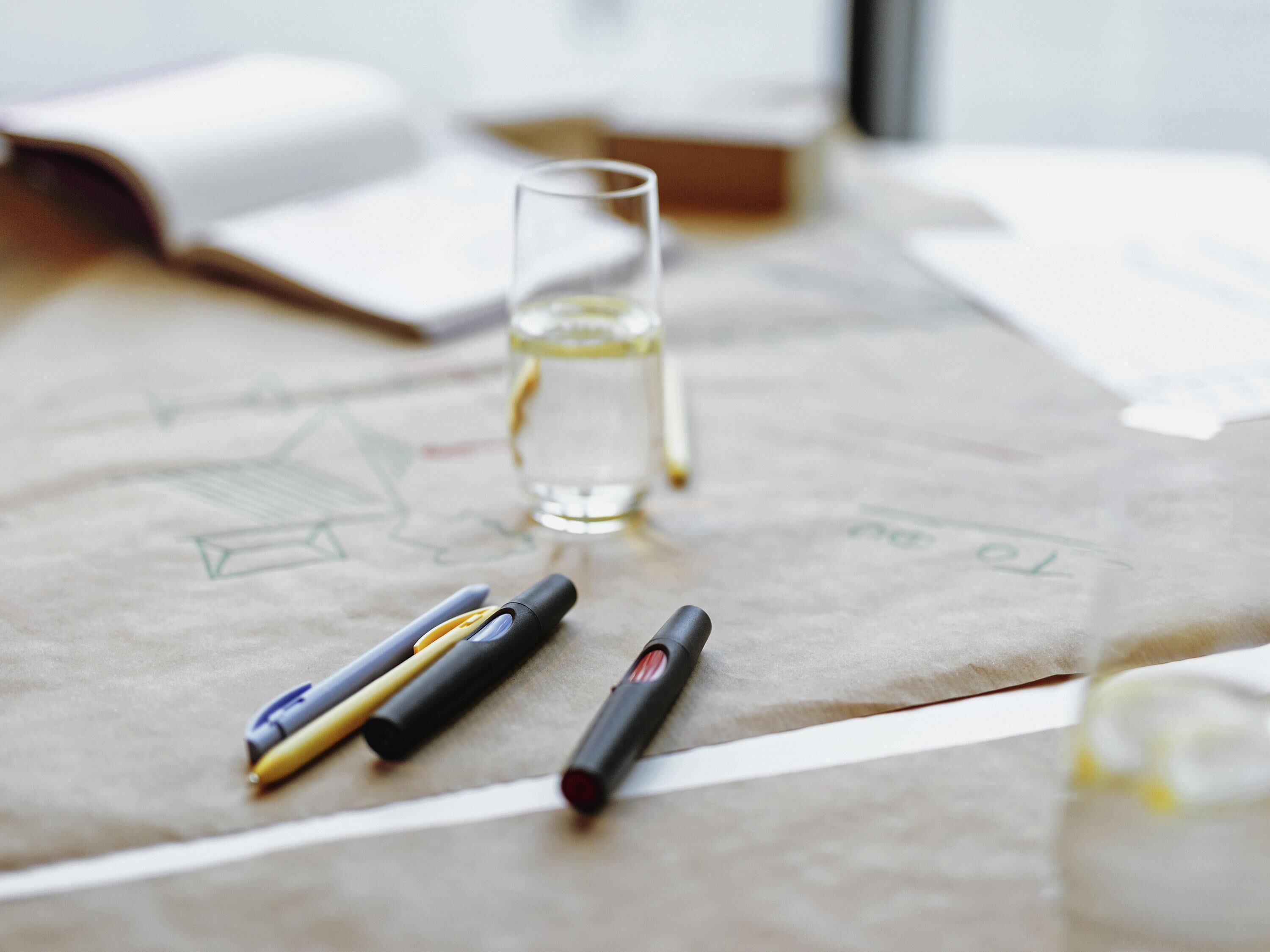 Et skrivebord med et glas vand, en kuglepen og en notesbog.