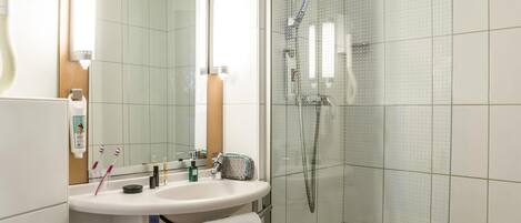 A modern bathroom with a glass shower enclosure, a white sink with a mirror above it, and toiletries on the sink.