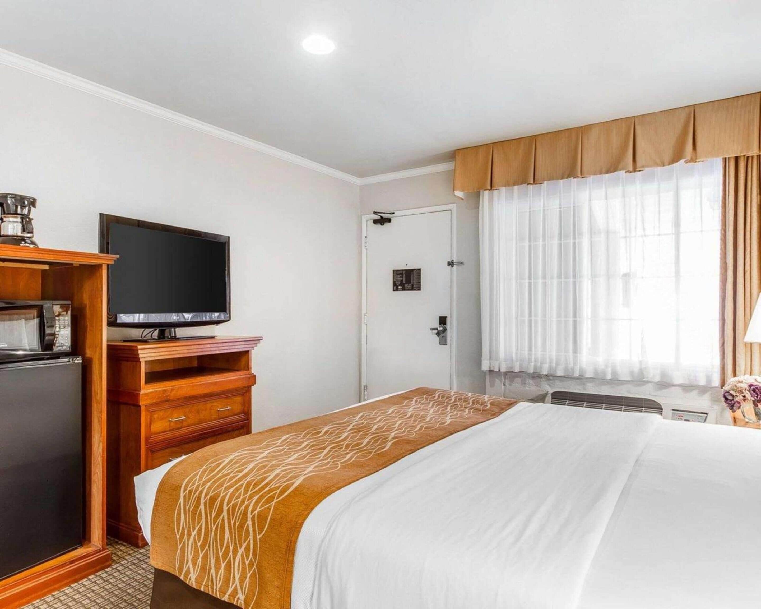 A hotel room with a bed, a television, a minibar, and a door.