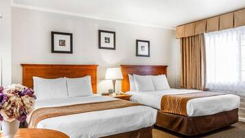 Habitación de hotel con dos camas, una mesita de noche con lámpara, un jarrón con flores y cuadros en la pared.