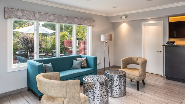 A modern living room with a teal sofa, a beige armchair, and two patterned side tables.