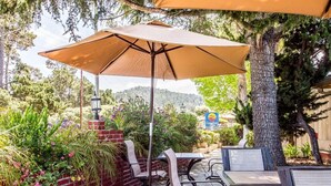 An outdoor patio area with tables and chairs, a large umbrella, and a brick wall with plants.