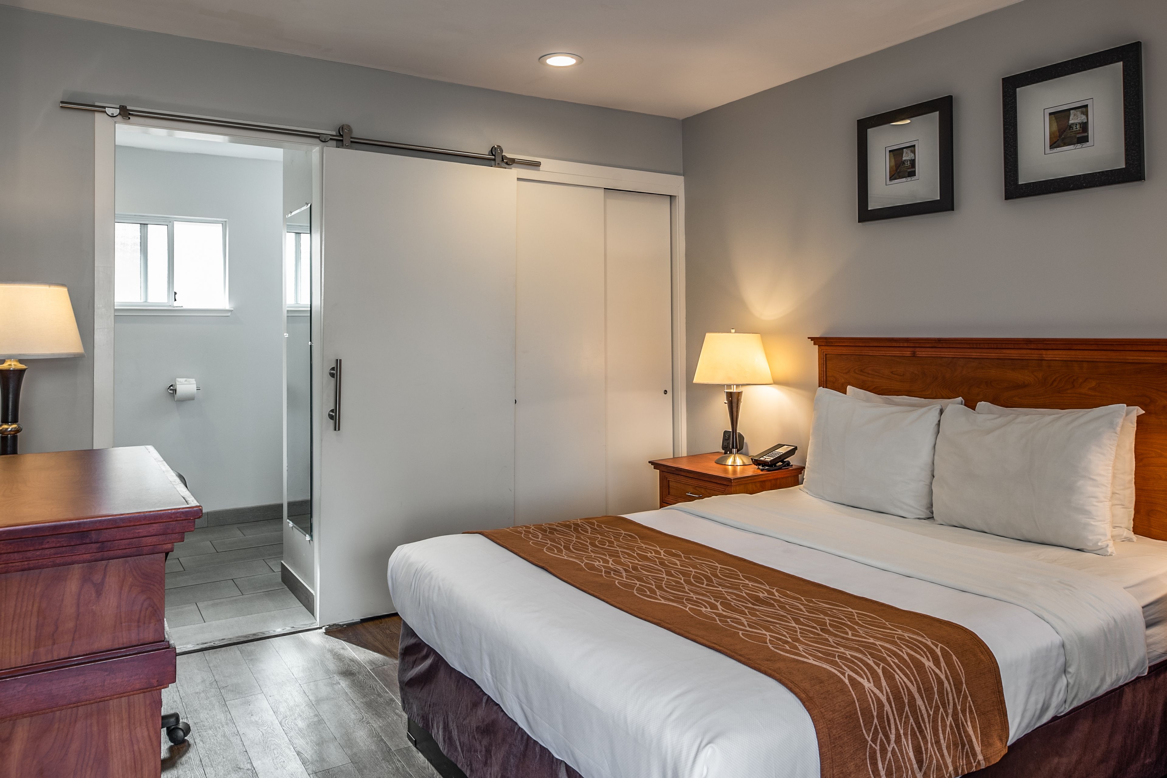 Une chambre d’hôtel comprenant un lit, une table de chevet, une lampe et une porte coulissante donnant accès à la salle de bain.