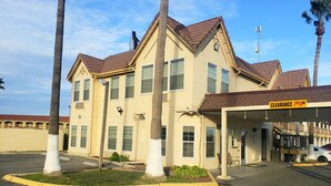 A two-story building with a beige facade and brown roof, featuring a covered parking area and a sign that reads "CLEARANCE 7TH AVE." - Days Inn by Wyndham Westley (Westley)