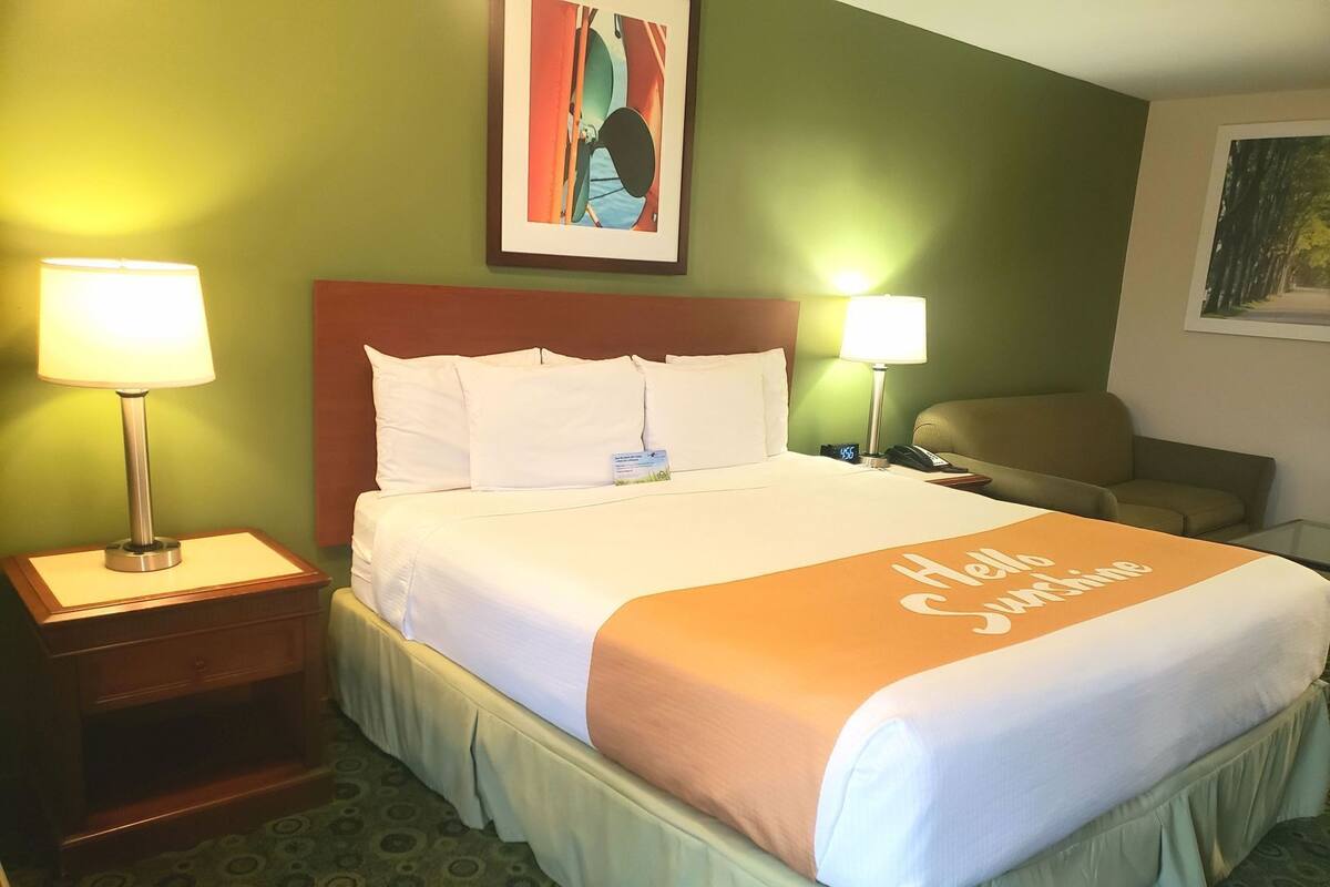 A hotel room with a bed, two bedside lamps, a nightstand, a chair, and a painting on the wall.