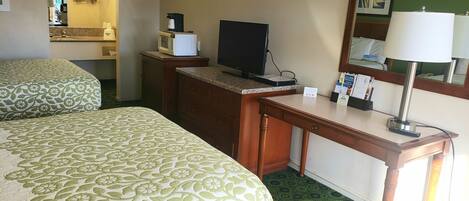 A hotel room with two beds, a desk, a television, a coffee maker, and a mirror.