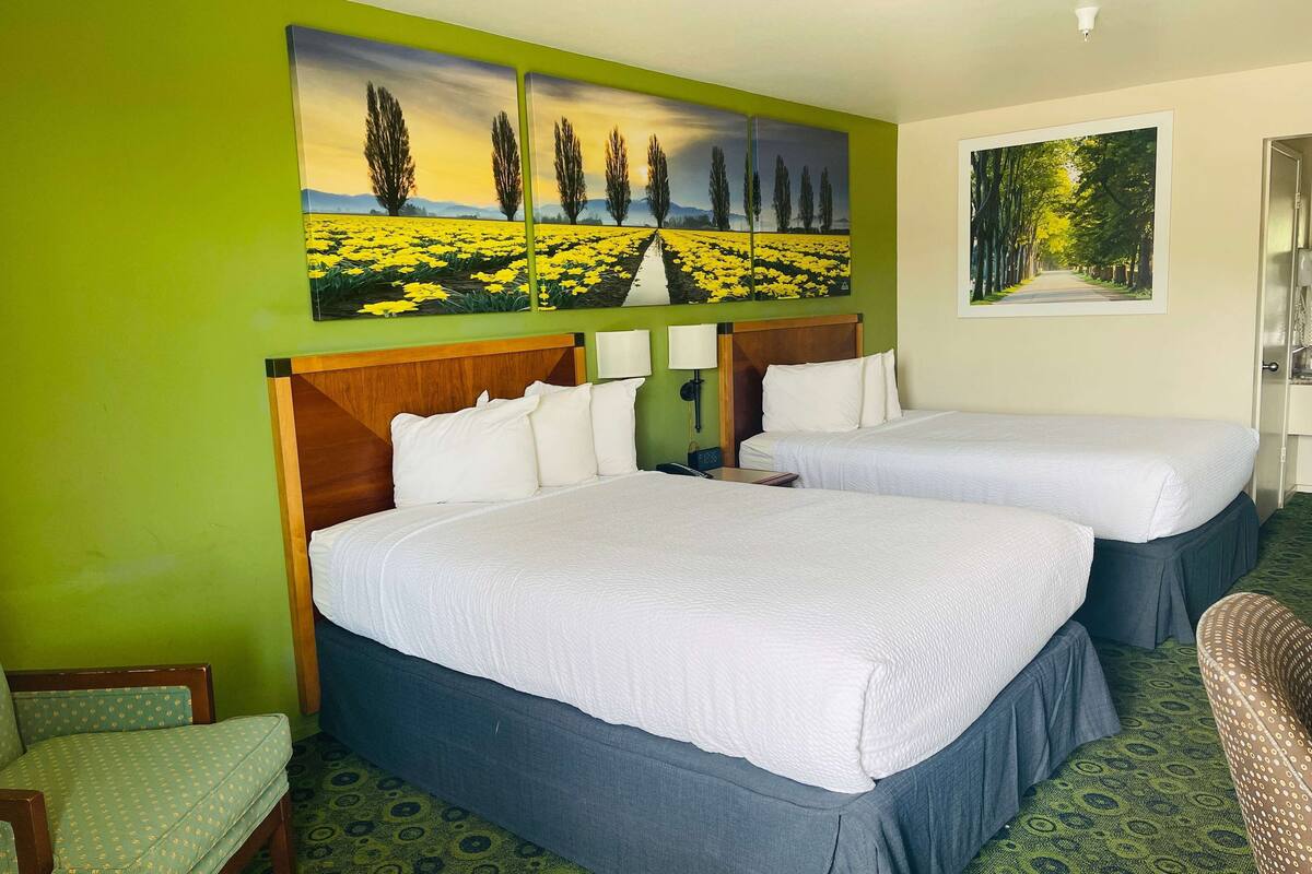 A hotel room with two beds, a green wall, and a large painting of a field.
