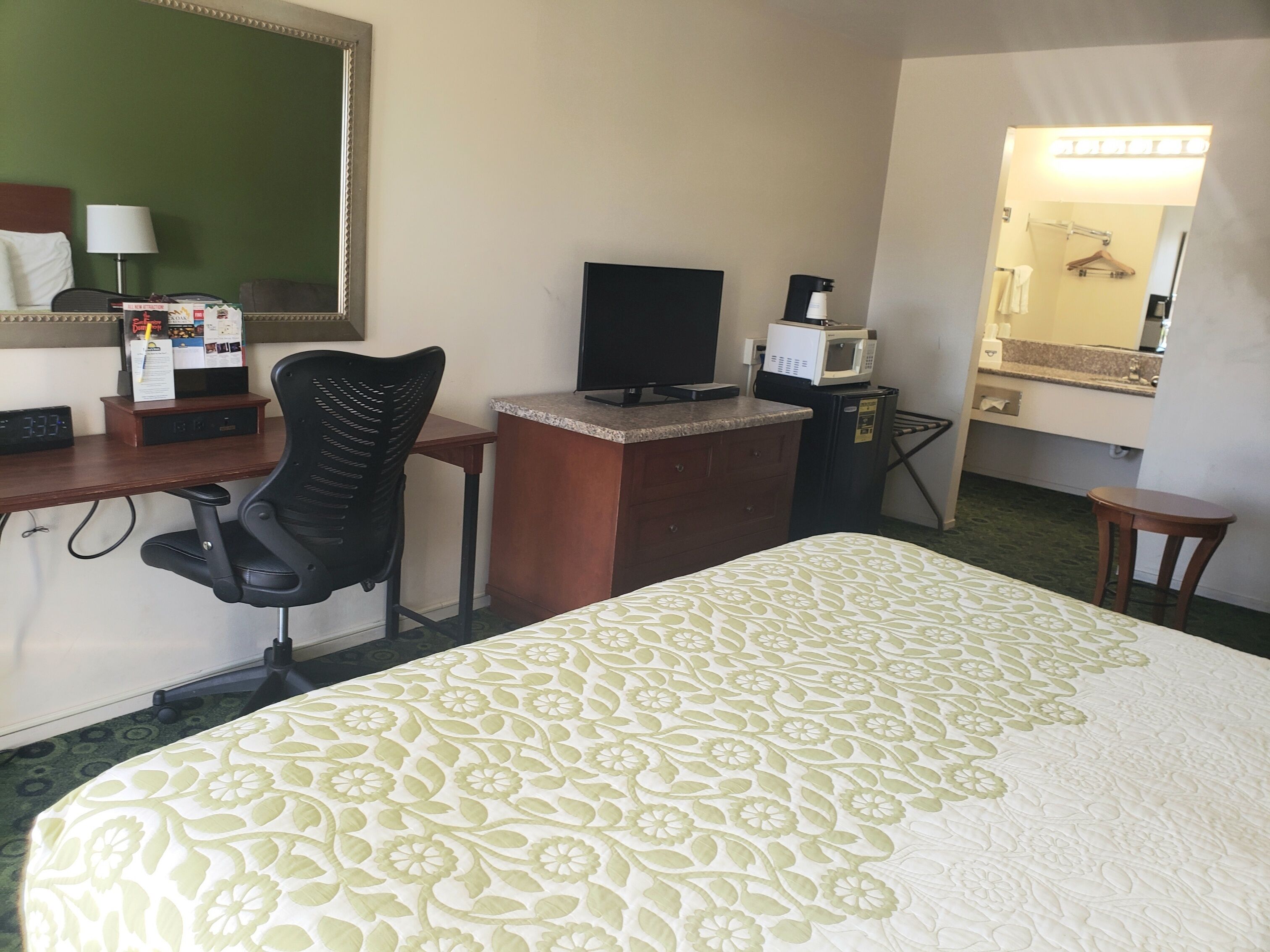 Habitación de hotel con cama, escritorio con computadora, silla, microondas, mesita y espejo.