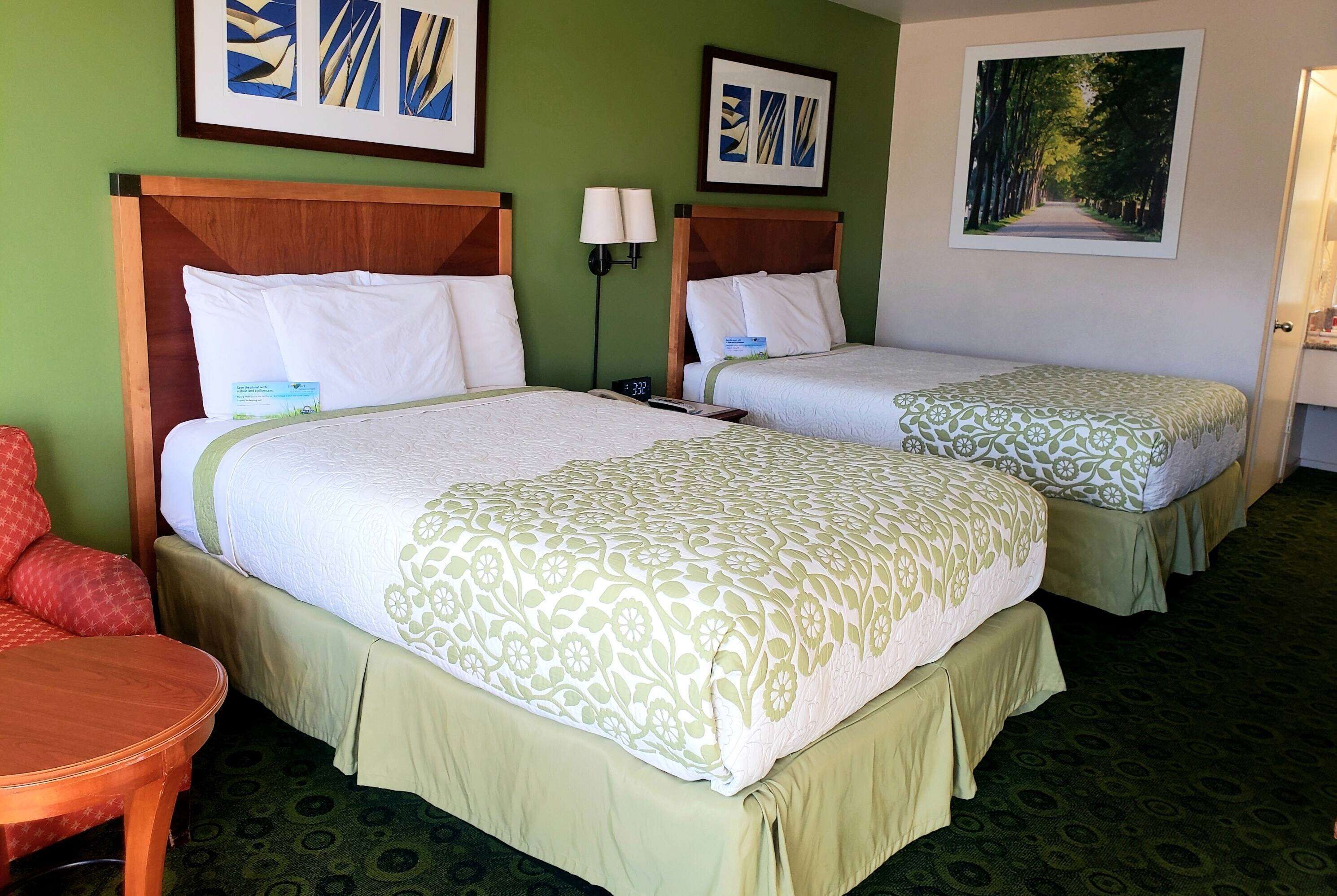 A hotel room with two beds, green walls, and artwork on the walls.