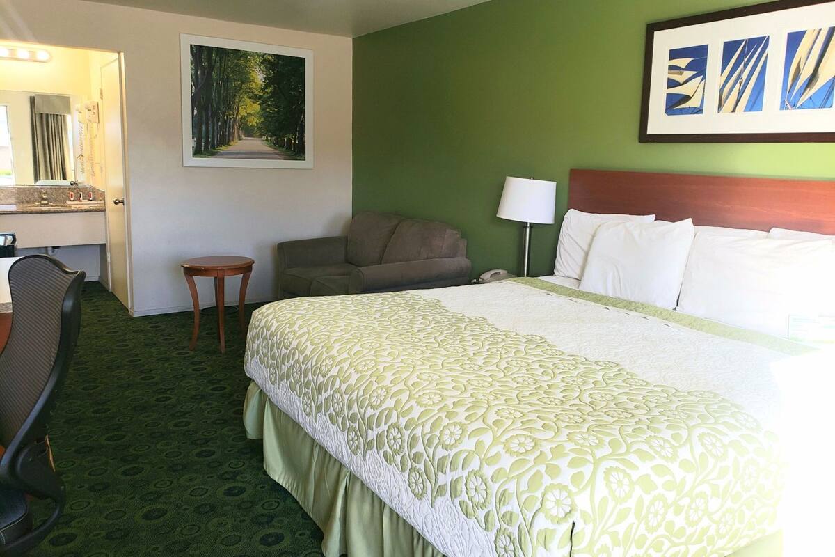 A hotel room with a bed, a desk, a chair, a lamp, and a painting on the wall.