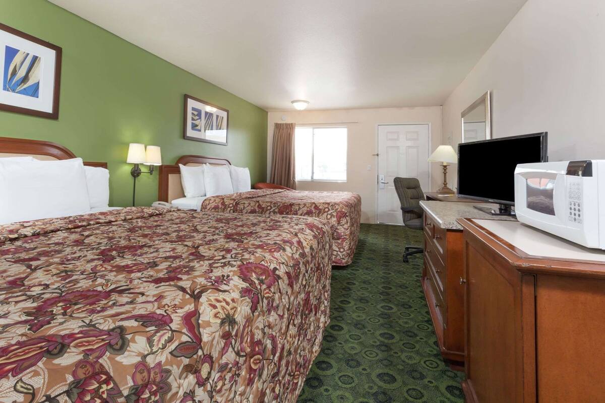 A hotel room with two beds, a television, a microwave, and a desk.