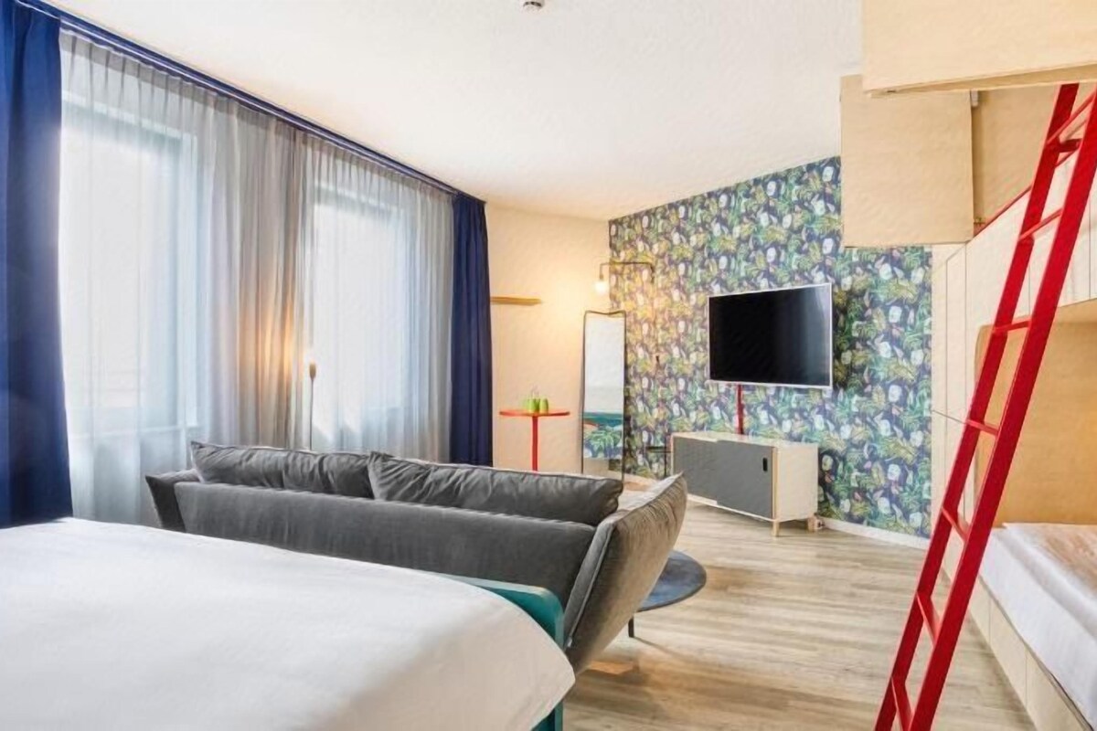 Una camera d'albergo con un letto, un divano, una TV e una scrivania.