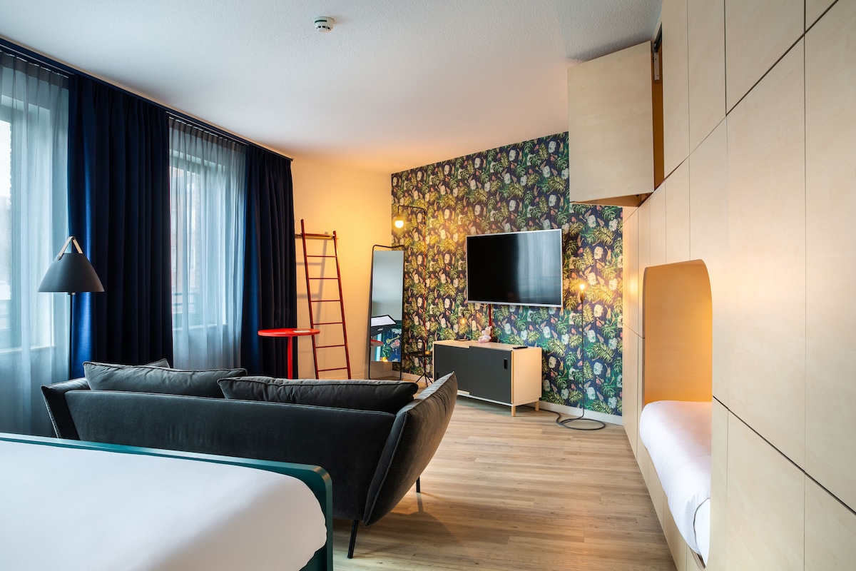 A modern hotel room with a sofa, a bed, a TV, and a desk.