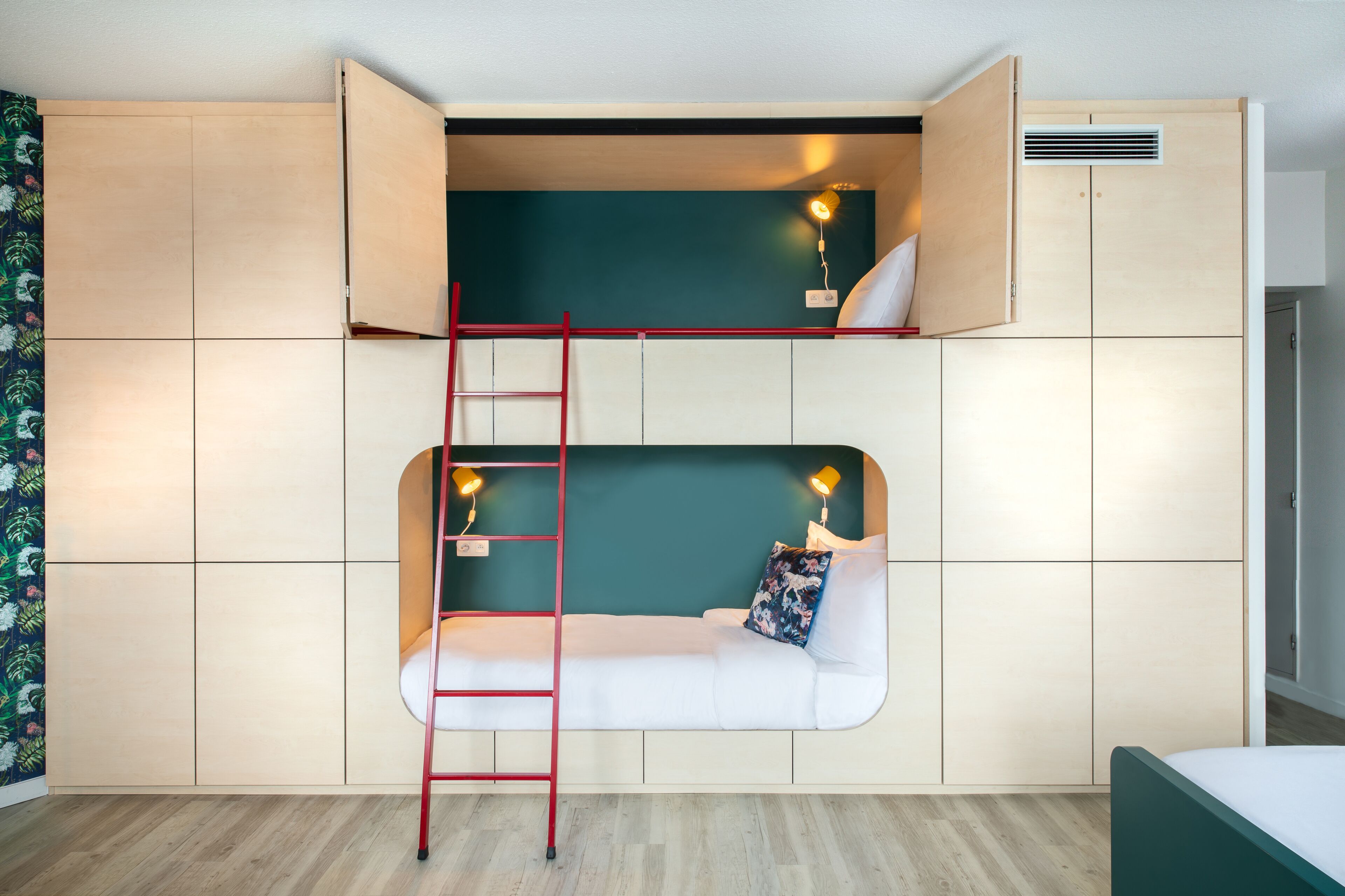 Een slaapkamer met een stapelbed, een ladder, twee bedlampjes en een klein plankje.