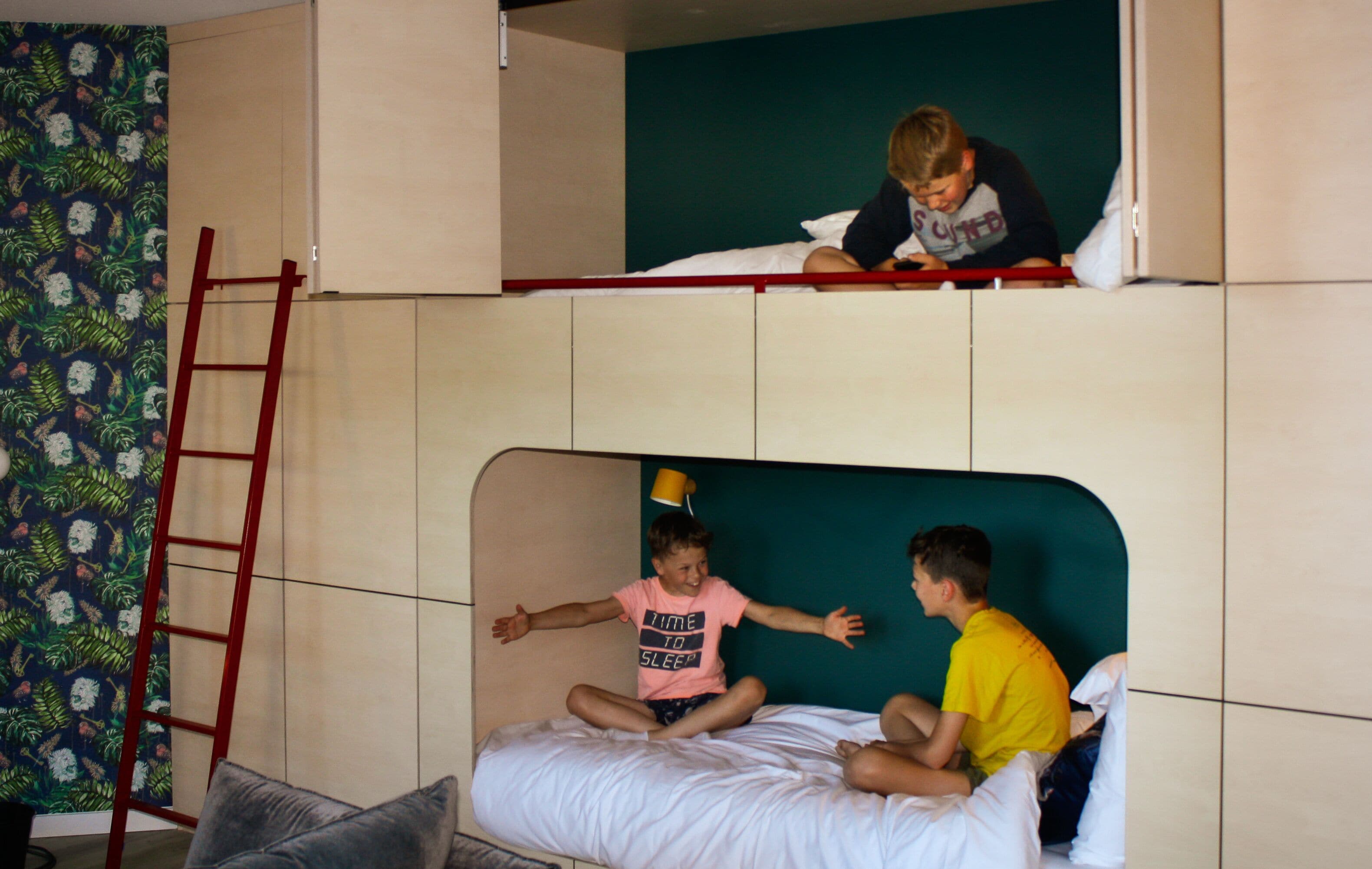 A bunk bed room with a ladder, a green wall, and a floral wallpaper on one side.