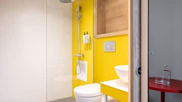 A bathroom with a yellow wall, a white toilet, a glass shower enclosure, and a red sink.