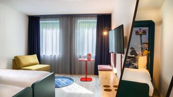 A hotel room with a bed, a sofa, a small table with a lamp, and a TV.