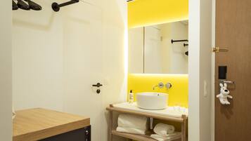 A modern bathroom with a wooden vanity, a white sink, and a yellow accent wall.