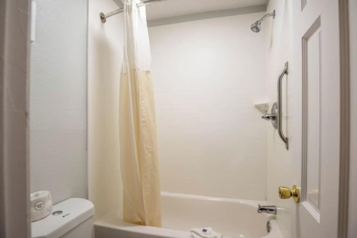 A bathroom with a bathtub, shower, toilet, and a door with a handle.