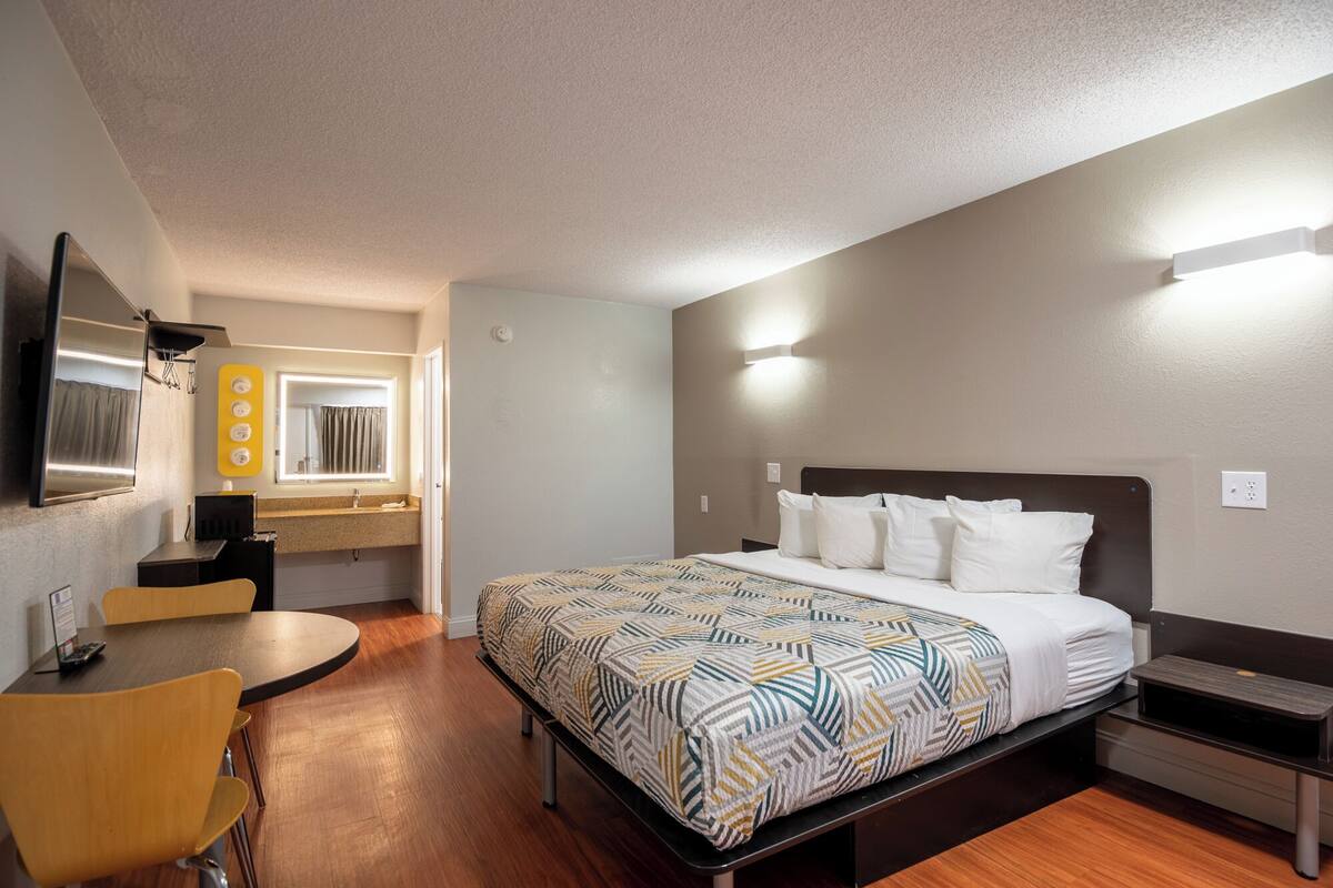 A hotel room with a bed, a desk, a chair, a mirror, and a window.