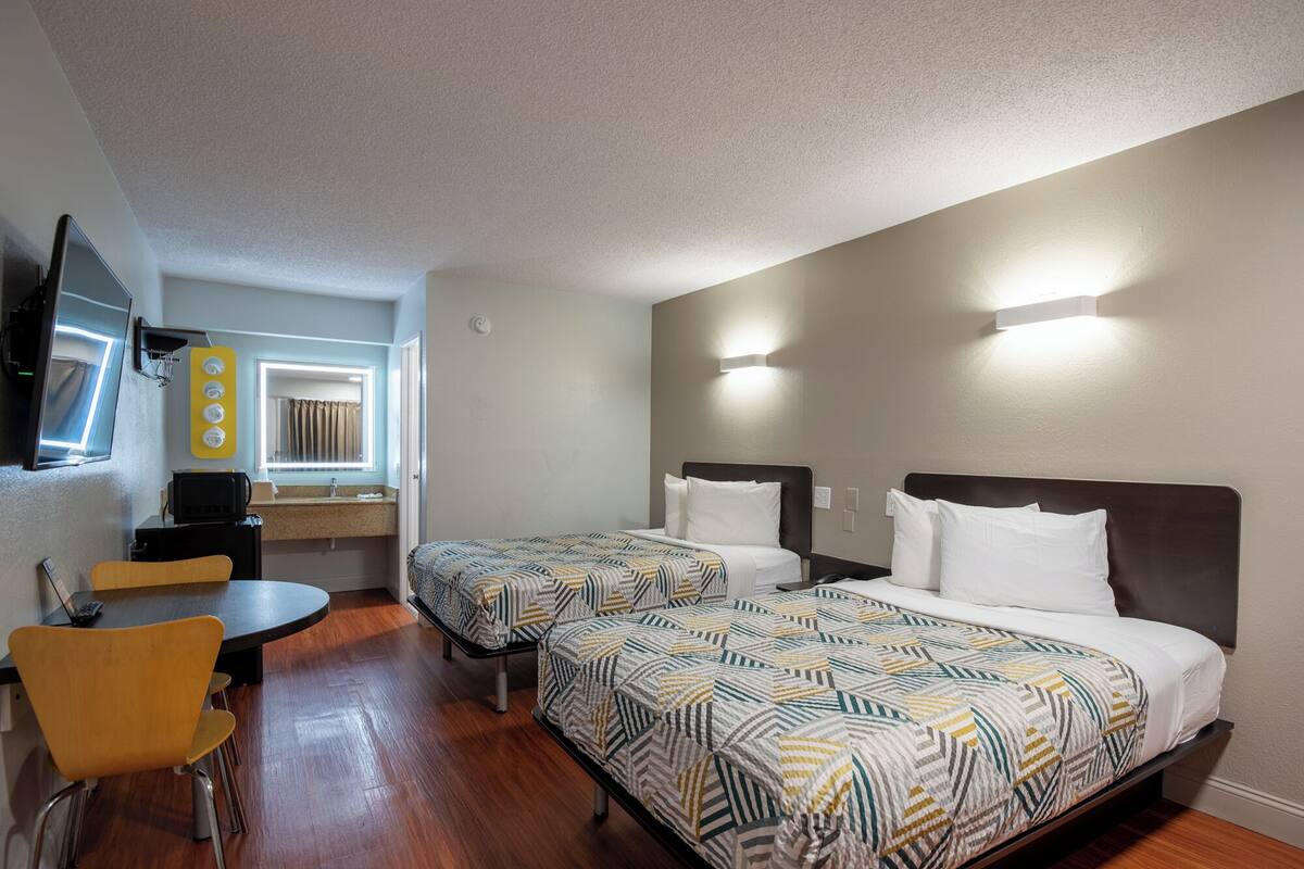 A hotel room with two beds, a desk, a chair, a TV, and a bathroom.