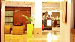 A hotel lobby with a reception desk, a large potted plant, and wicker furniture. - Accra City Hotel (Accra)