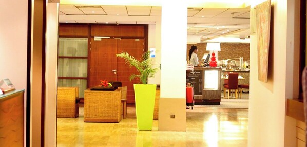 A hotel lobby with a reception desk, a large potted plant, and wicker furniture.