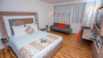 Habitación de hotel con una cama grande, un sofá, un escritorio con silla y un minibar.