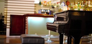 A piano in a room with a bar area in the background.