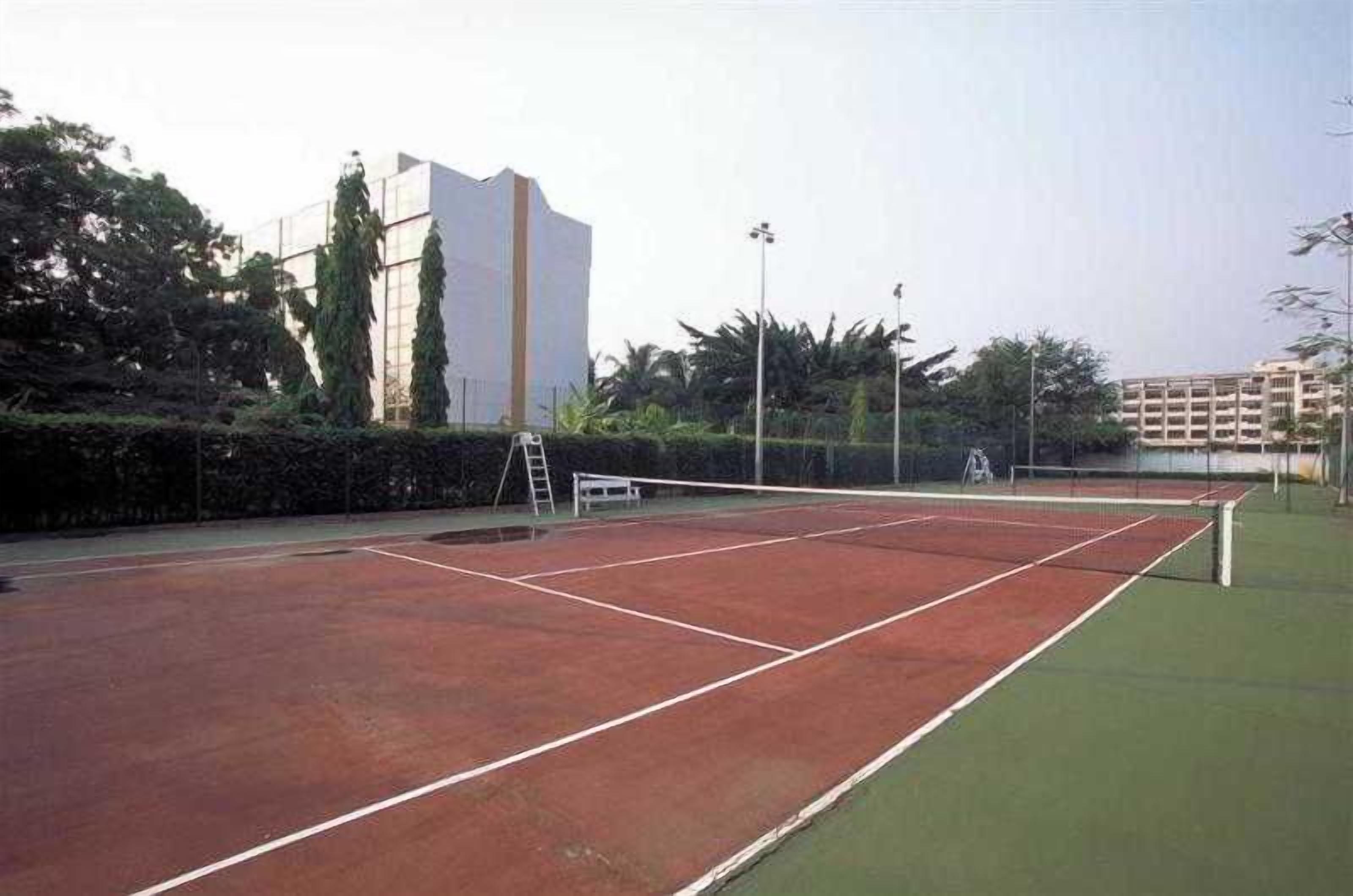Una cancha de tenis con una red, rodeada por una valla y edificios al fondo.