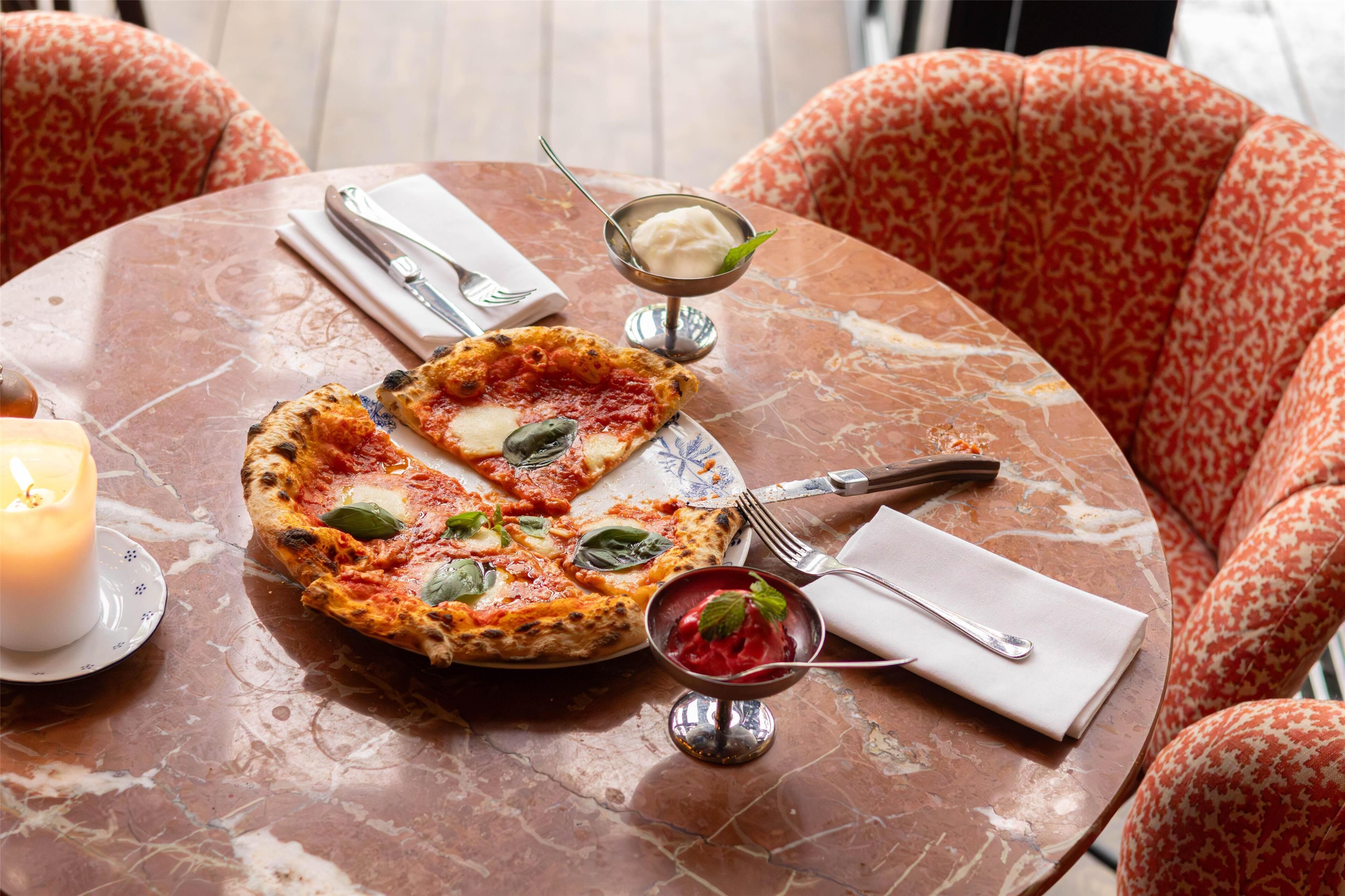 A table with a pizza, a candle, and two small bowls of dessert.