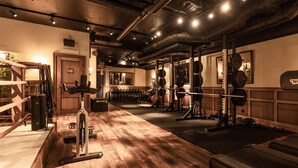 Une salle de sport avec un plancher en bois, du matériel d’entraînement en musculation et un miroir au mur.