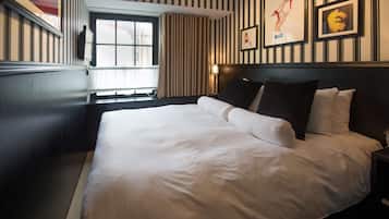 Una cama bien hecha con sábanas blancas en una habitación de hotel con papel tapiz a rayas y una ventana con cortinas.