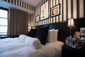 A hotel room with a large bed, striped wallpaper, and framed artwork on the wall.