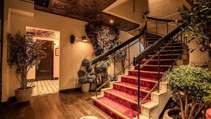 Un escalier dont les marches sont recouvertes d’une moquette rouge, avec une rampe en bois et des plantes en pot.