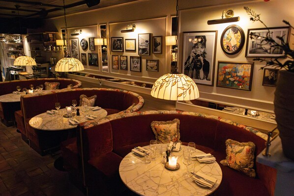 A restaurant with round tables, red cushioned booths, and wall-mounted lamps.
