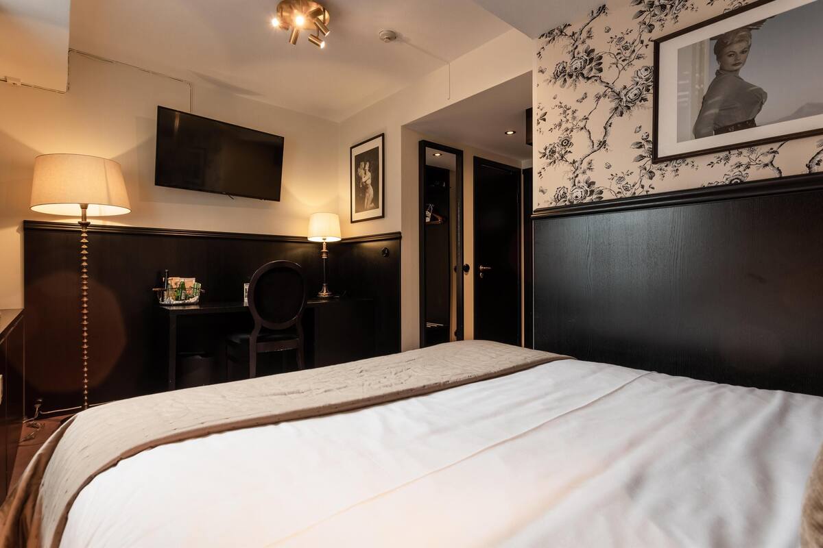 A hotel room with a large bed, a desk, two lamps, a television, and a framed picture on the wall.
