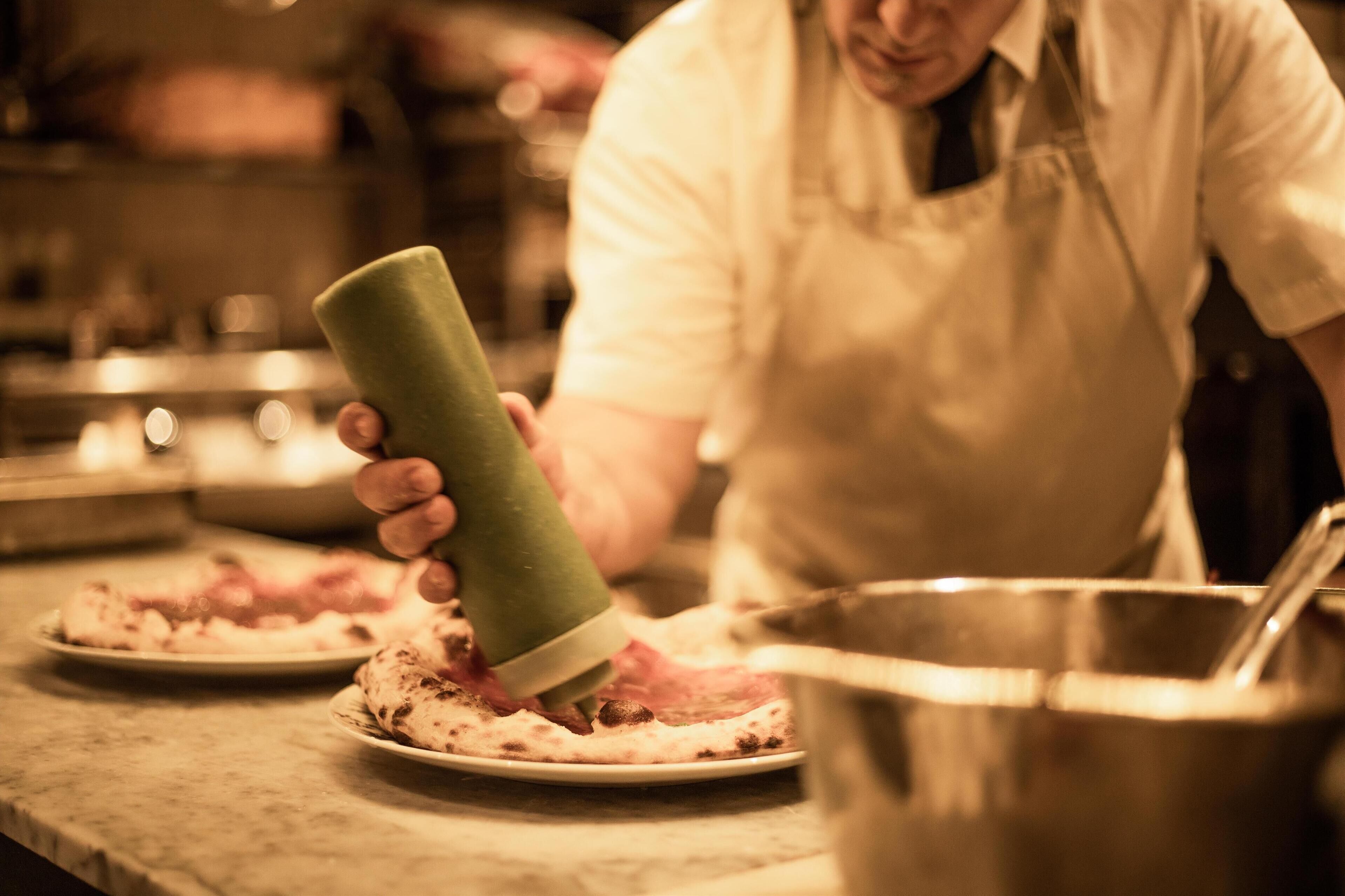A person in a kitchen preparing food, holding a green container, with a pot and plates on the counter.