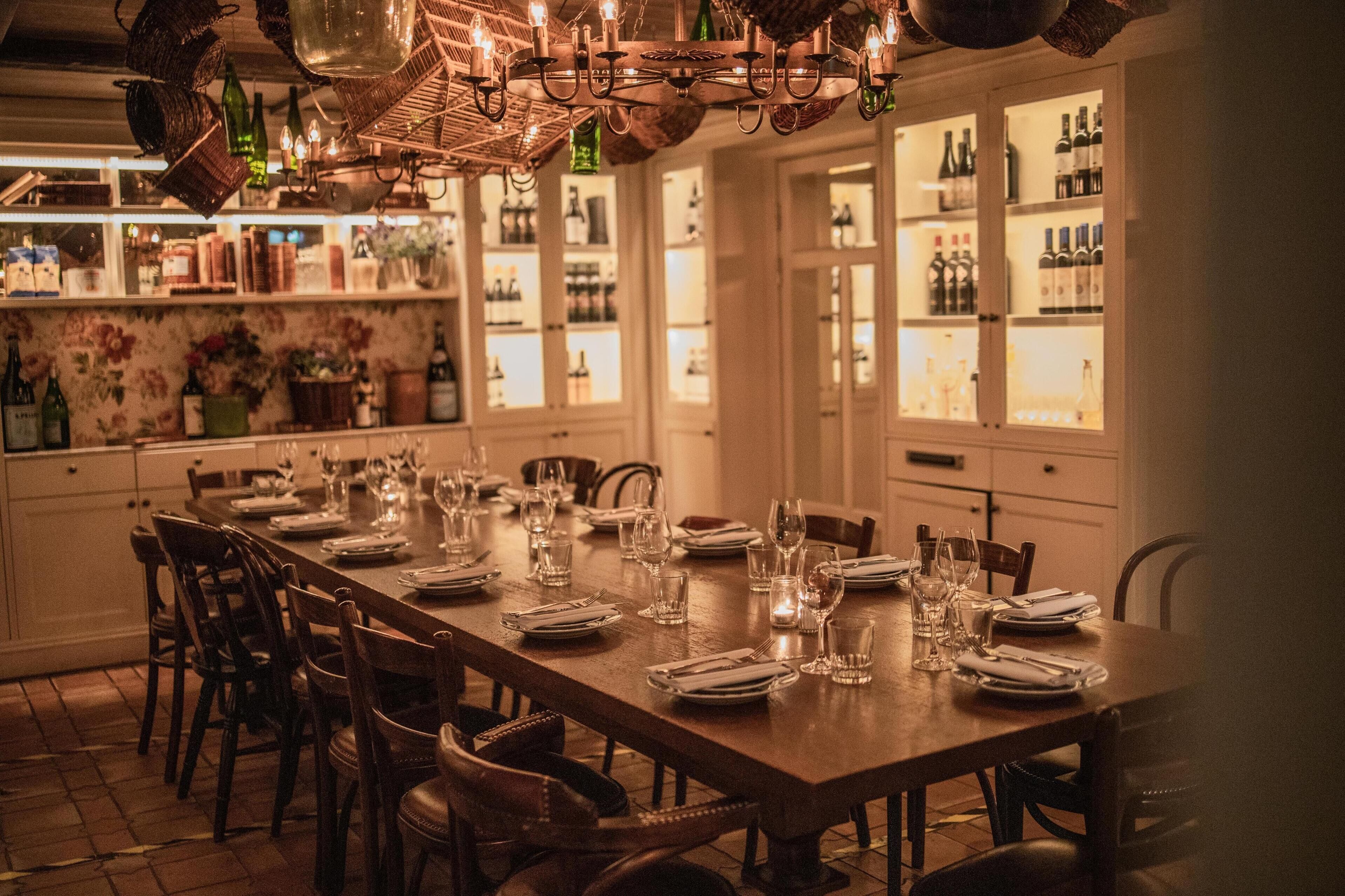 A dining area with a long wooden table set for multiple people, surrounded by chairs.