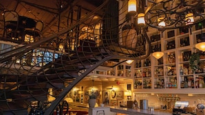 Un espace bar doté d’un escalier en colimaçon, d’étagères remplies de bouteilles et d’un comptoir avec une caisse enregistreuse.