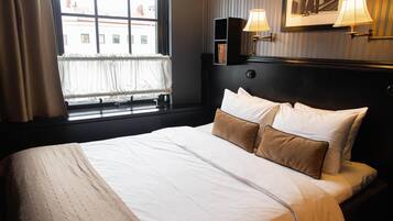 Una habitación de hotel con una cama grande, una ventana con cortinas, una estantería y lámparas fijadas a la pared.