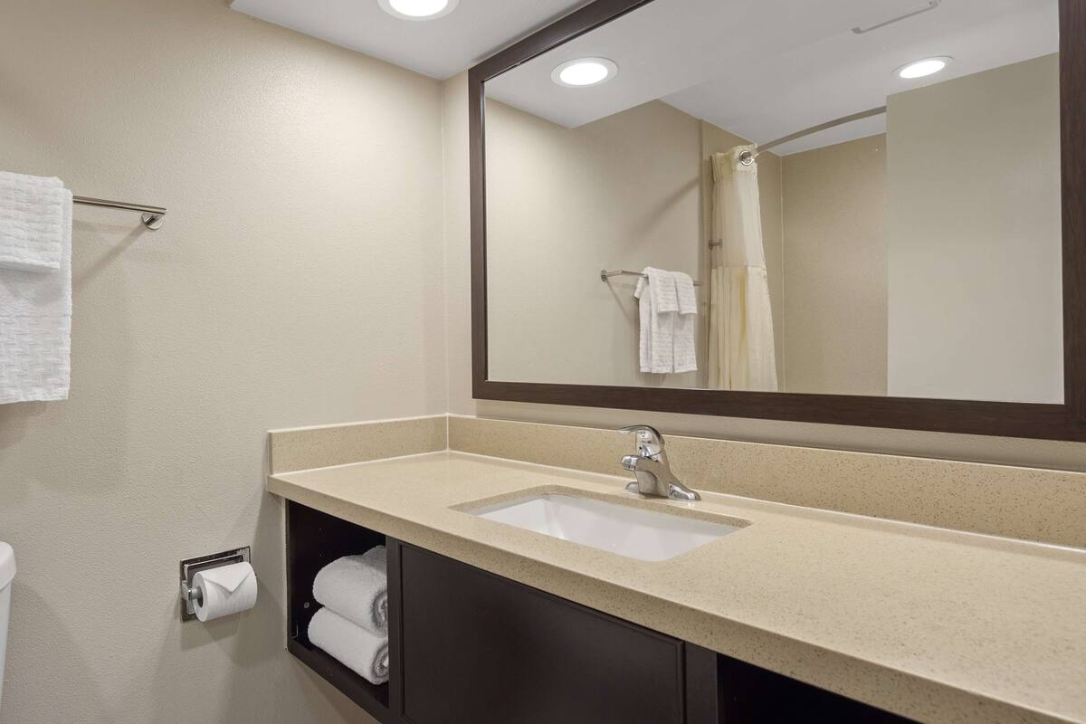 A bathroom with a sink, mirror, towel rack, toilet, and a towel dispenser.